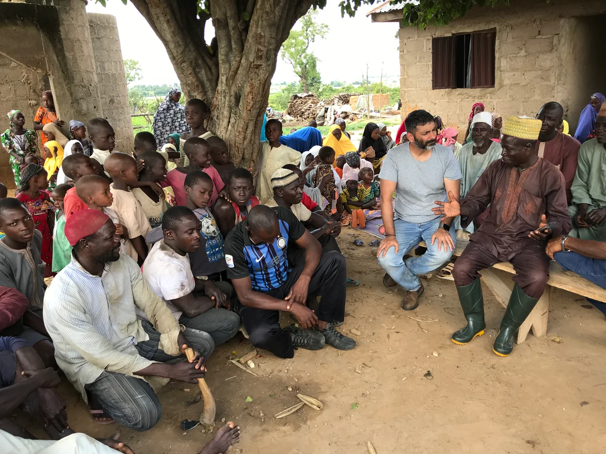 Community townhall dialogue with village elders and farmers under tree shade